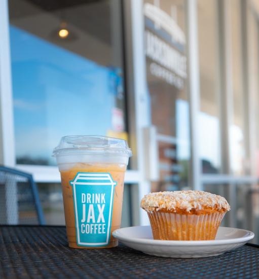 A coffee with a "Drink JAX Coffee" sticker on the cup and a muffin