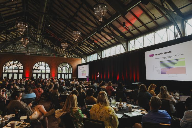 An audience sitting at a table and watching a larger session at Tourism Academy