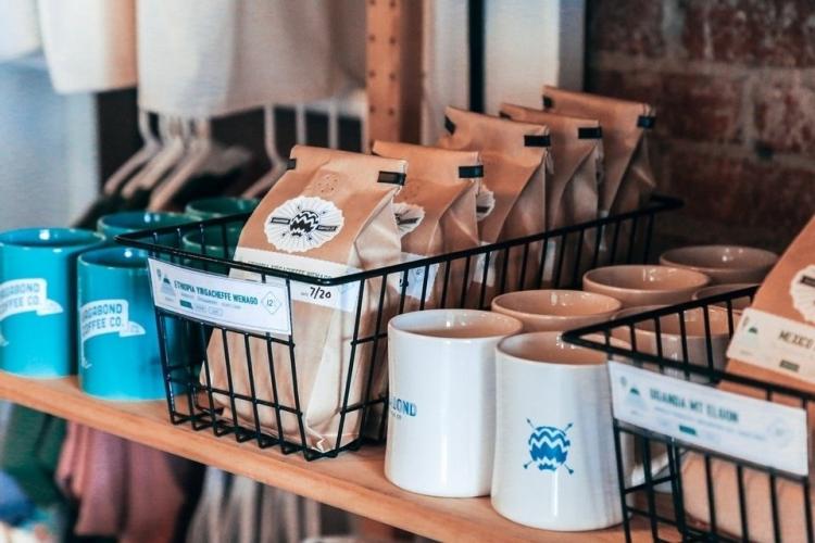 Wooden shelves lined with blue and white mugs and bags of coffee from Vagabond Coffee in Jacksonville, Florida.