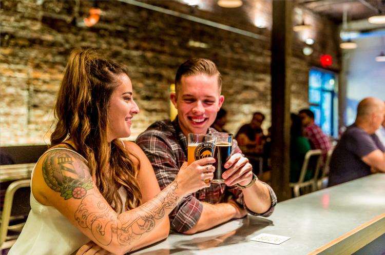A man and woman clink their glasses together at a bar.