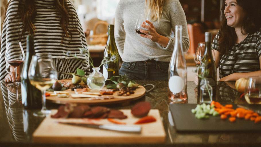 A group of women drinking and eating by a table covered in food and wine glasses.